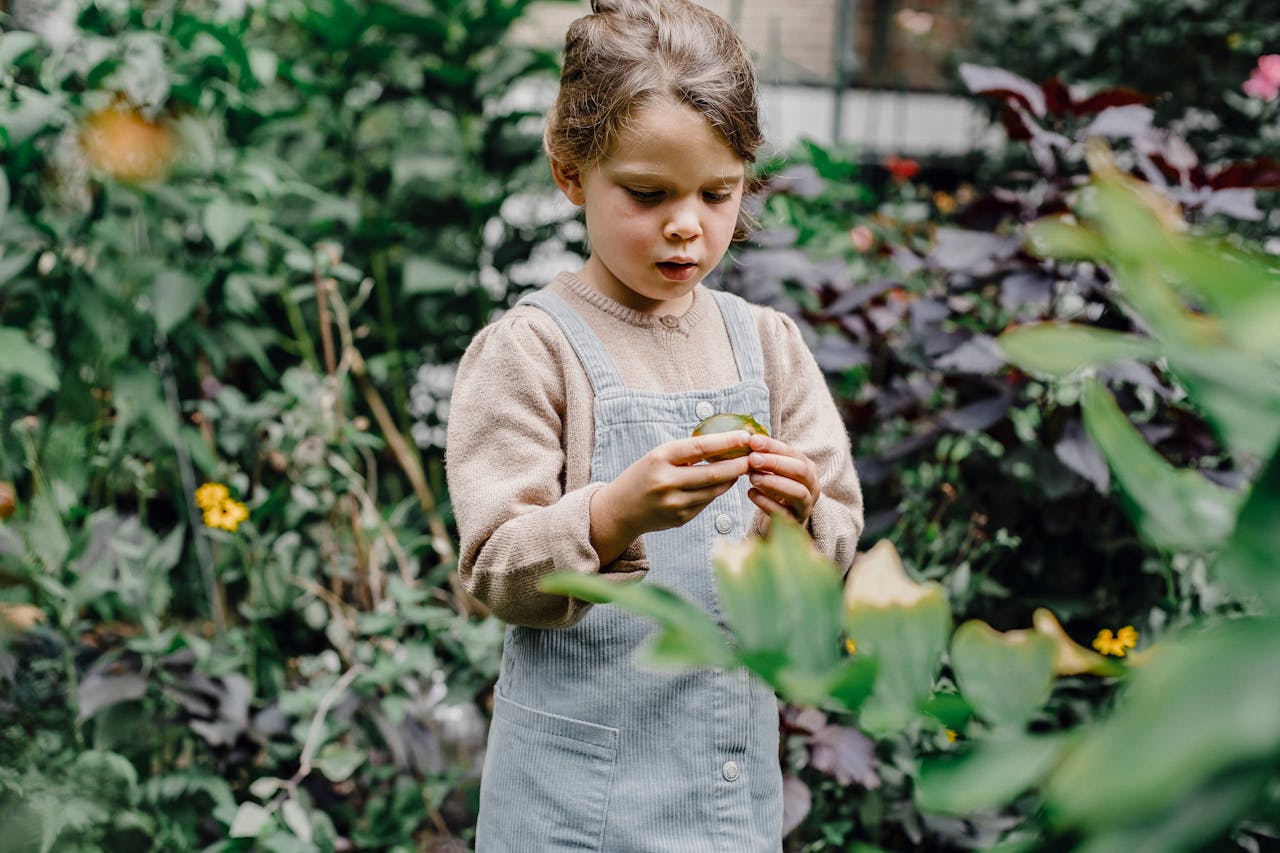 Über uns A young girl enjoys exploring fresh foliage in a lush garden setting, highlighting the beauty of nature.
